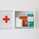 CLICswab Packung „Hautpflege durch desinfizierende Wirkung“ griffbereit in einem geöffneten weißen Erste-Hilfe-Wandschrank neben Verbandsmaterial.