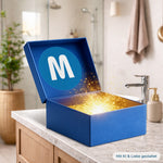 Geöffnete blaue MediaShop Mystery Box Beauty auf einer Waschtischplatte im modernen Badezimmer, aus deren Innerem ein magisch goldenes Leuchten mit Glitzerpartikeln erstrahlt.