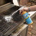 Pure100 NavyClean Allesreiniger wird mit einer Sprühflasche als weißer Reinigungsschaum direkt auf einen stark eingebrannten Grillrost gesprüht.
