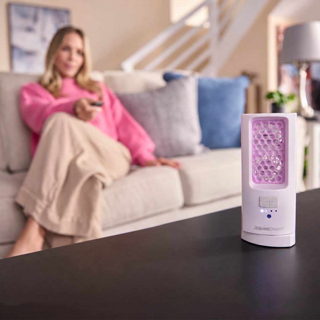 ScentDream Raumduftsystem auf einem Tisch mit eingesetztem violettem Lavendelglanz-Nachfüllpod; im Hintergrund sitzt eine entspannte Frau auf dem Sofa.
